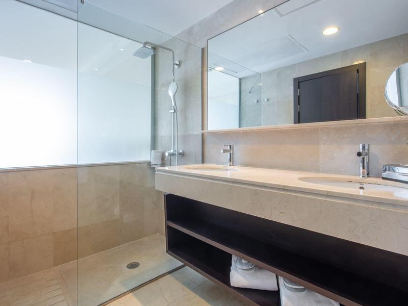 Moderní hotelová koupelna s béžovým sprchovým koutem a dvojitým umyvadlem se zrcadlem.