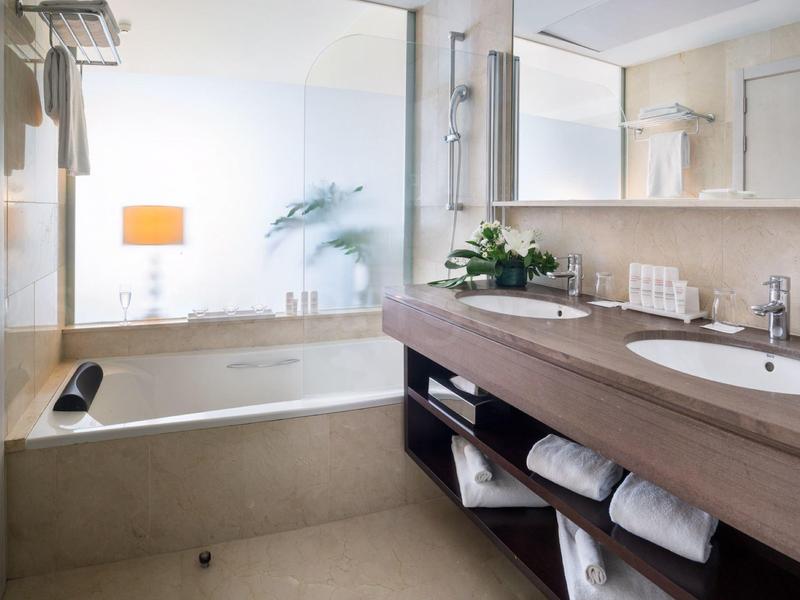 Moderní koupelna s vanou, umyvadlem, velkým zrcadlem a měkkými ručníky.