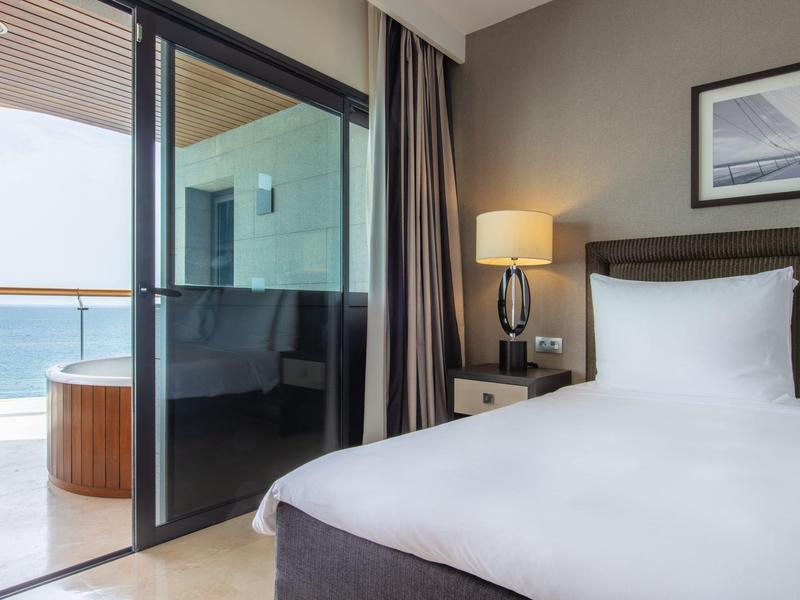 Moderní hotelový pokoj s velkou postelí a balkonem s výhledem na moře.