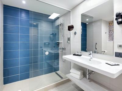 Moderne hotelbadkamer met grote douche, witte wastafels en blauwe tegels.