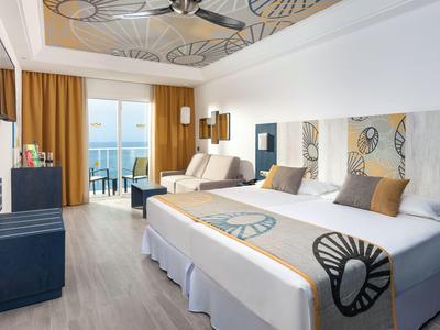 Moderne hotelkamer met tweepersoonsbed, zithoek en balkon met uitzicht op zee.