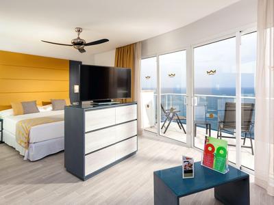 Modern hotelkamer met tweepersoonsbed, tv, balkon en zeezicht overdag.