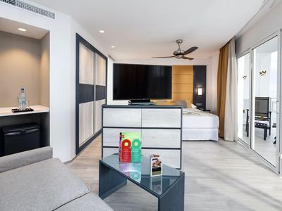 Modern hotelkamer met bed, tv, bank en balkon met glazen deuren.