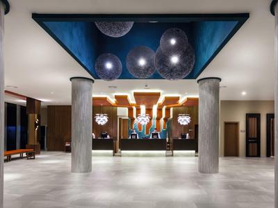 Loby moderna de hotel con columnas de concreto, techo artístico y área de recepción decorativa.