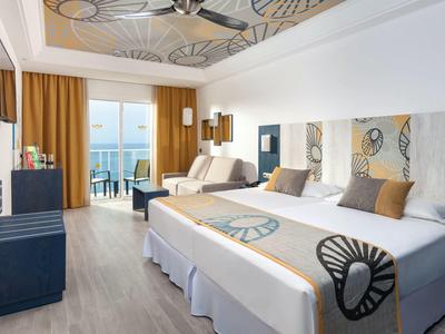 Habitación de hotel moderna con cama doble, balcón y vista al mar, decorada con estilo.