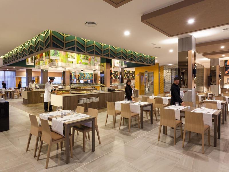 Restaurante moderno de hotel con mesas preparadas y área de buffet al fondo.