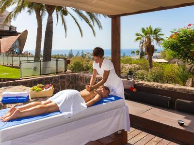 Mężczyzna otrzymuje masaż na leżance na zewnątrz z palmami i oceanem w tle.