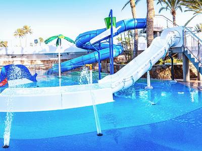 Zewnętrzny park wodny z niebieskimi zjeżdżalniami i płytkim basenem otoczonym palmami.