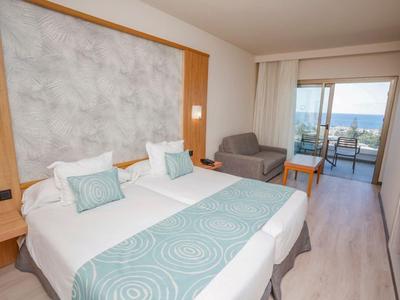 Jasny pokój hotelowy z dwoma łóżkami pojedynczymi, balkonem i widokiem na morze.