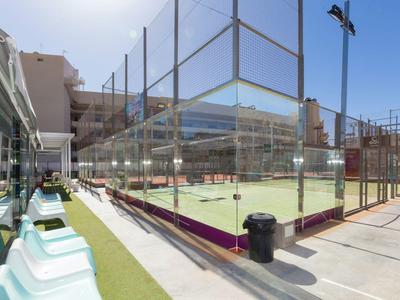 Pista de tenis moderna con asientos bajo cielo despejado, rodeada de edificios.