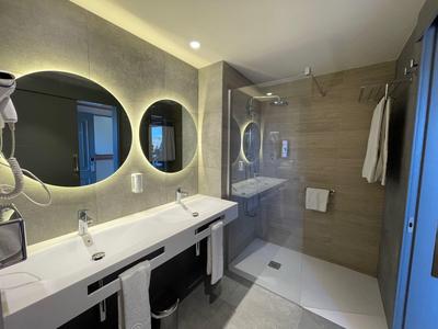 Nowoczesna łazienka z podwójną umywalką, okrągłymi lustrami, prysznicem i neutralnymi kolorami.