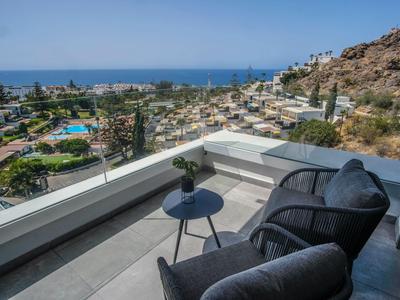 Balcón con dos sillones y una mesa pequeña con vistas al mar y una montaña al fondo.