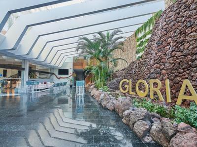 Nowoczesna lobby hotelowa z szklanym dachem, palmami i kamienną ścianą z napisem GLORIA.