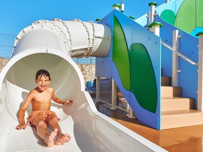 Chłopiec zjeżdżający z białej zjeżdżalni wodnej w parku wodnym w słoneczny dzień.