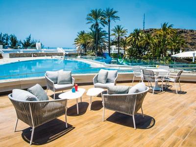 Strefa wypoczynkowa na zewnątrz z nowoczesnymi krzesłami i stołem przy basenie, otoczona palmami.