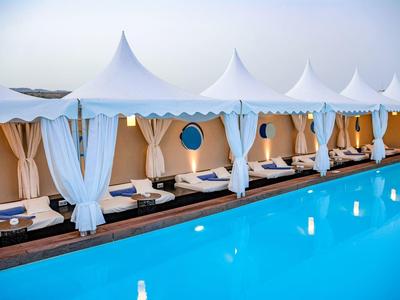 Białe kabany przy basenie z zasłonami i leżakami obok czystego, niebieskiego basenu.