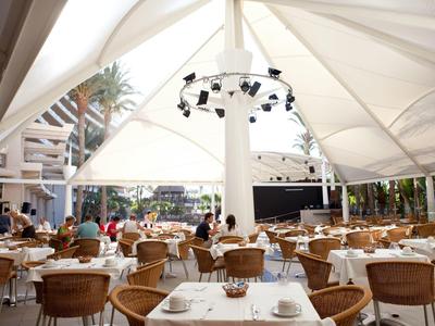 Restauracja na zewnątrz hotelu z wiklinowymi krzesłami i stołami pod dużym białym namiotem.