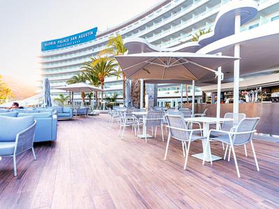 Strefa zewnętrzna z stolikami, krzesłami i parasolami na drewnianym tarasie nowoczesnego hotelu.