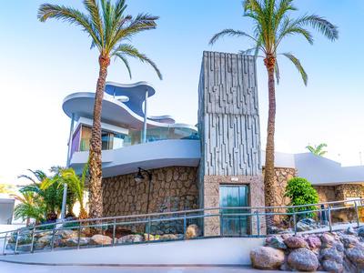 Nowoczesne wejście do lobby hotelowego z kamiennymi ścianami, szklanymi drzwiami i palmami.