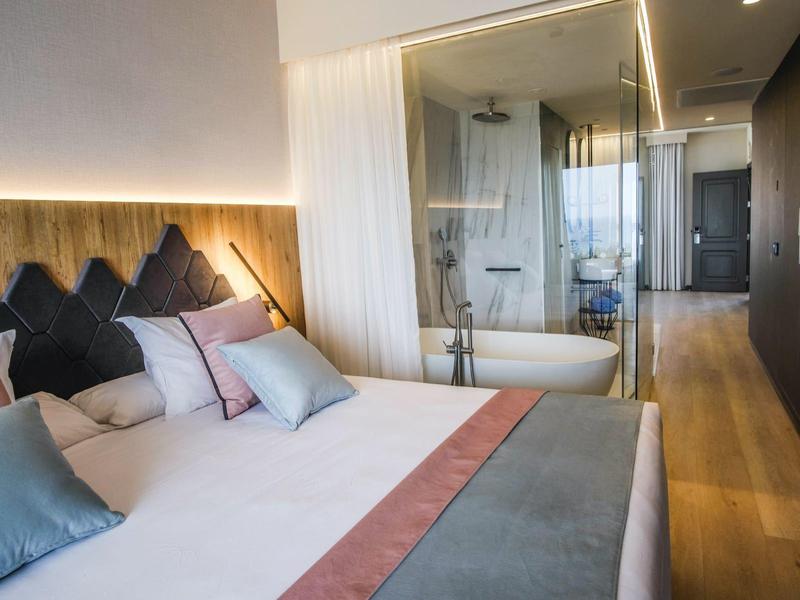 Nowoczesny pokój hotelowy z dużym łóżkiem, dekoracyjnymi poduszkami i przegrodą łazienkową ze szkła.