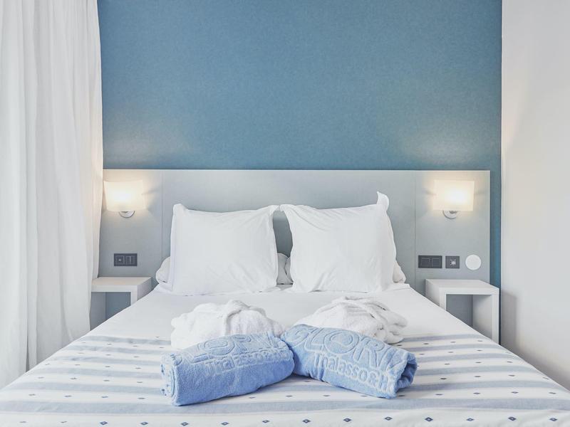 Jasny pokój hotelowy z niebieską ścianą, białą pościelą i niebieskimi ręcznikami na łóżku