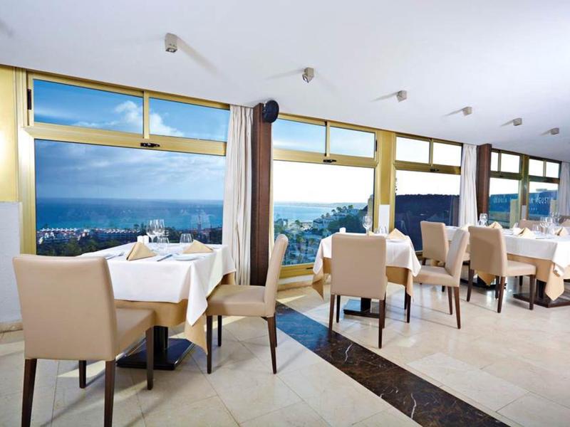 Jasna jadalnia z dużymi oknami z widokiem na morze i stołami przykrytymi białymi obrusami.