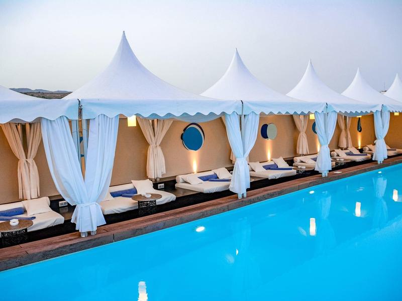 Białe kabany przy basenie z zasłonami i leżakami obok czystego, niebieskiego basenu.