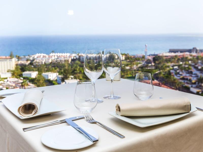 Stół nakryty dla czterech osób na tarasie z widokiem na morze i marinę o zachodzie słońca