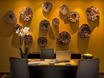 Moderner Arbeitsplatz mit zwei Laptops, Stühlen, Pflanze und dekorativen Holzskulpturen an gelber Wand.