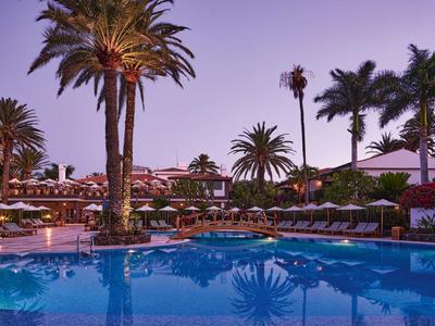 Avondzicht op een zwembad met verlichte palmbomen en ligstoelen in een resort.