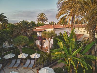 Hotel area with lounge chairs, umbrellas, and lush tropical plants at sunset.