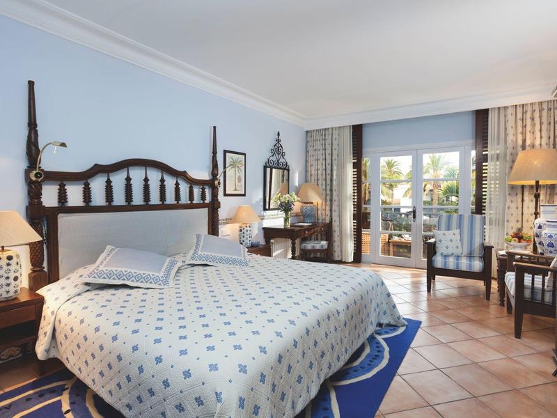 Helles Schlafzimmer mit großem Bett, Holzmöbeln, Teppich und Terrasse mit Gartenblick.