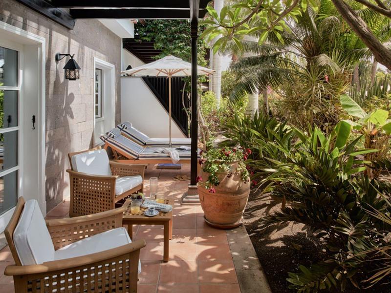 Terrasse mit Holzstühlen, Tisch, Sonnenschirm und grünen Pflanzen im Garten bei Tageslicht.