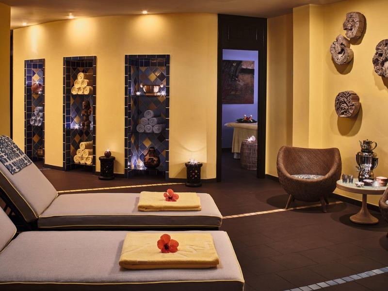 Gemütlicher Wellnessraum mit Liegen, Handtüchern und Wanddekoration aus Masken.