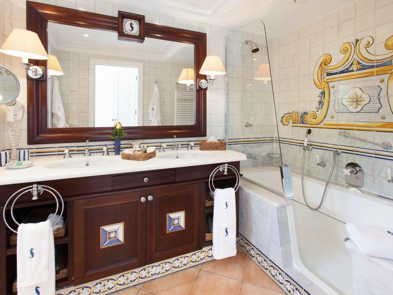 Helles Badezimmer mit Holzschrank, großem Spiegel, weißer Badewanne und dekorativen Wandfliesen.