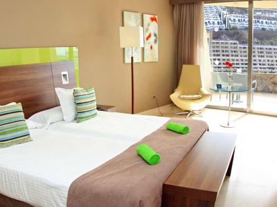 Licht hotelkamer met tweepersoonsbed, groen-witte accenten en uitzicht op een terras.
