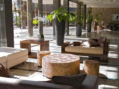 Lichte hotel lounge met sofa's, houten tafels en grote ramen voor veel daglicht.