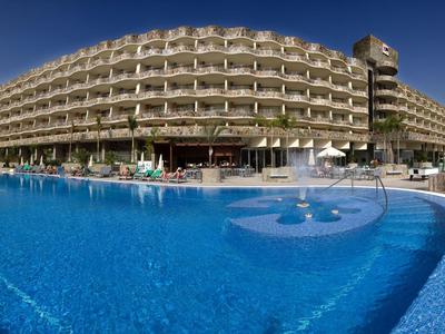 Großes Hotel mit Balustraden und großem blauen Swimmingpool bei klarem Himmel.