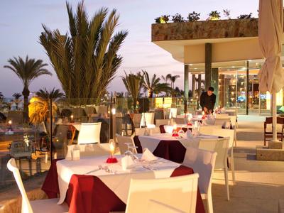 Elegant buitenrestaurant van hotel met witte tafelkleden en palmbomen bij zonsondergang.