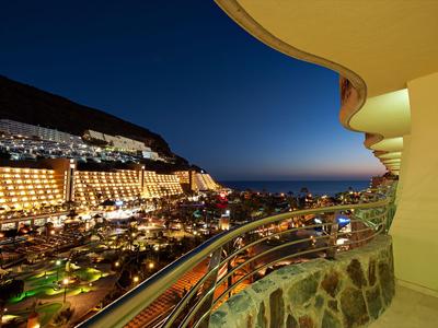 View from a hotel balcony overlooking lit buildings and the sea at night.