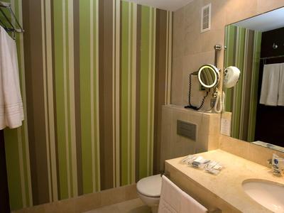 Modern hotel bathroom with green striped wall and beige countertop.