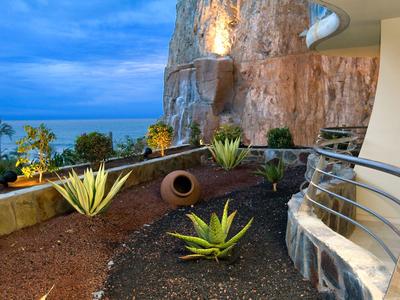Terrace with plants and sea view by a rock wall under a clear sky.