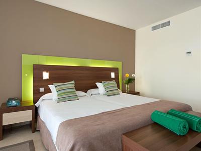 Modern hotel room with large bed, green accent, and two green towels.