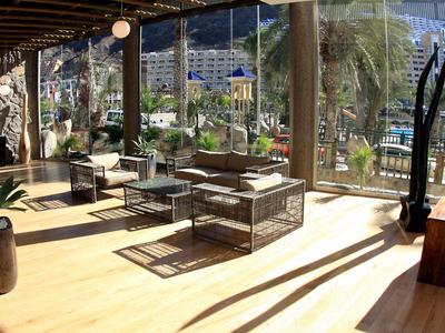 Modern hotel room with wooden floor, seating area, and large panoramic window with mountain view.