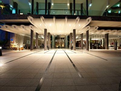 Modern hotel met verlicht entreegebied en open paviljoen 's nachts.
