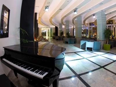 Hotel lounge met zwarte vleugelpiano en moderne zithoeken op een lichte vloer.