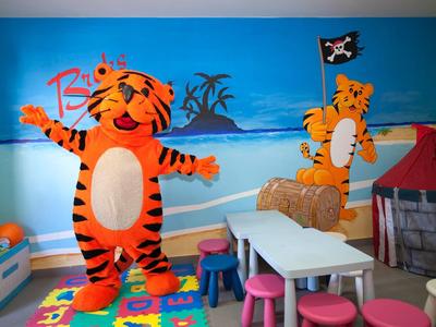 Kinderkamer met kleurrijk tapijt, witte tafels, roze krukjes en tijgermaskottes.