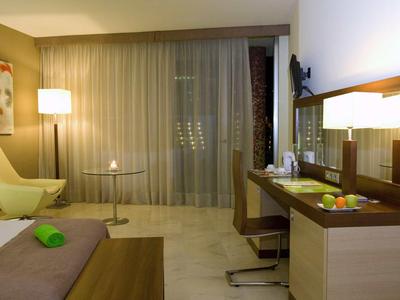 Modern ingerichte hotelkamer met bureau, fauteuil, lamp en balkon.