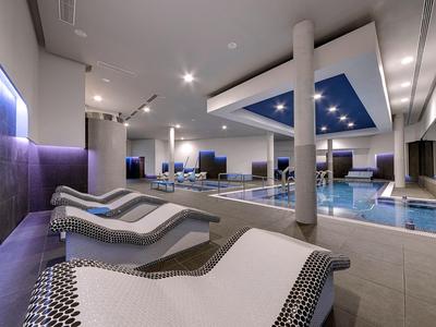 Área moderna de bienestar con piscina climatizada, columnas y tumbonas con iluminación tenue.