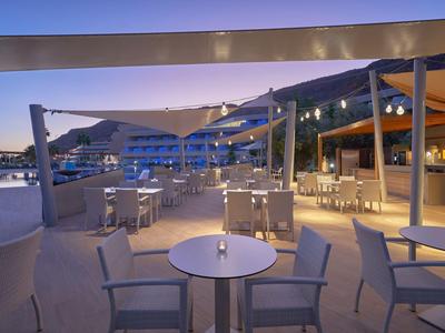 Evening outdoor view of a modern hotel terrace with tables, chairs, and lighting.